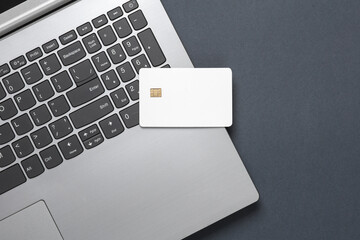Laptop and white blank bank card with chip on dark background. Template for design. Online shopping