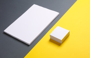 White sheets of a4 paper and square memo paper stack on a yellow-gray background. Template for design