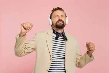 french man in blazer and neck scarf listening music in wireless headphones isolated on pink.