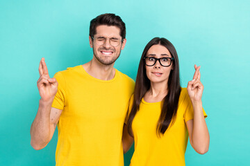 Photo of two young nervous people panic crossed fingers wait bite lips expectation wear glasses please isolated on aquamarine color background