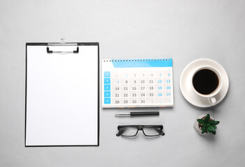 Clipboard with a blank sheet of paper and coffee cup, calendar, office accessories on gray background. Flat lay