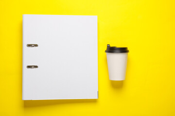 Coffee cup with binder folders on yellow background. Business concept. Top view