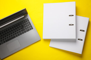 Laptop with binder folders on yellow background. Business concept. Top view - obrazy, fototapety, plakaty