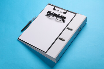 Clipboard with binder folder, eyeglasses on blue background. Business concept