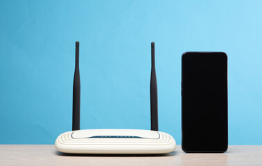 Dual antenna wi-fi router with smartphone on the table, blue background - obrazy, fototapety, plakaty