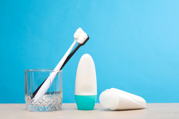 Two toothbrushes in a glass and antiperspirants on the table, blue background
