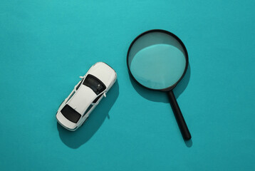 Toy car model and magnifying glass on blue background