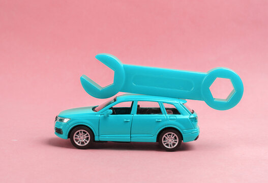 Toy car model with a wrench on pink background. Auto service, repair concept.