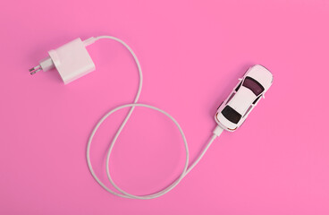Toy model of an auto with a charger on a pink background. Electric car