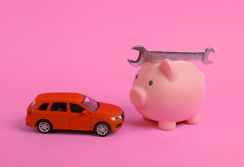 Toy car model with wrench and piggy bank on a pink background. Auto service, repair concept.