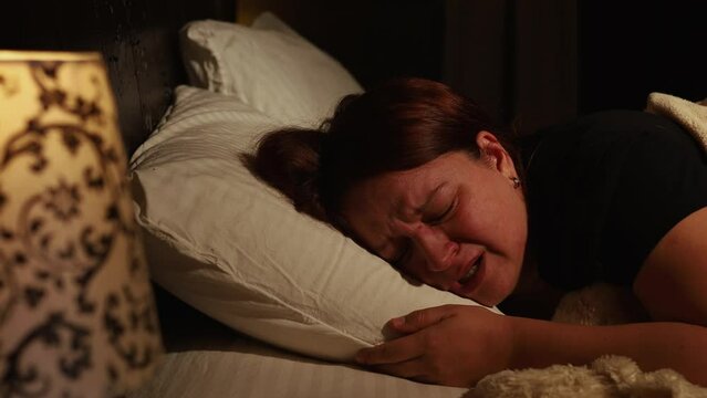 Distressed woman lie on pillow in bed and cry bitterly in dark bedroom. Splash out emotions, sob with tears. Emotional breakdown, stress, sufferings. Depression, night hysterics before sleep.