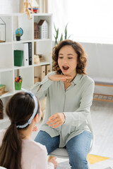 Speech therapist opening mouth and gesturing near blurred pupil in consulting room.