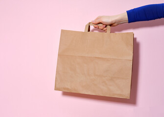 Female hand holding a paper bag with delivered items. Pink background