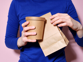 Woman dressed in bright blue t-shirt holding food delivery packaging