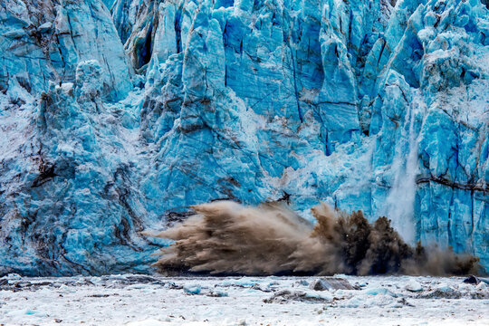 Calving ice falls off a glacier and into the water below.