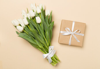 White tulip bouquet and gift box on color background, top view