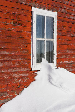 A Snow Drift Touching The Window Along A Building With A Red Painted Wooden Facade That Is Worn And Weathered; Orion, Alberta, Canada