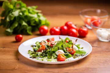 Plate of healthy classic close-up caprese salad with mozzarella cheese tomatoes and basil in kitchen - italian cuisine