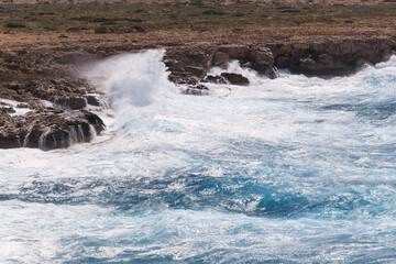 Big waves in the ocean hit the rocks on the shore with big splashes. Light blue water in the sea during a storm