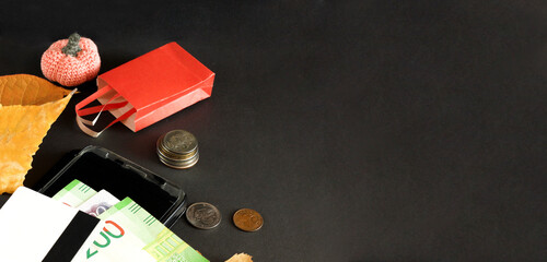 autumn sale layout on dark background, black friday, shopping basket next to coins and bills, orange pumpkins made of yarn and leaves, online shopping