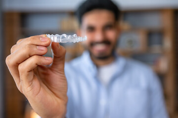 Man showing an invisible silicone aligner for dental correction. Male hand holding the plastic braces dentistry retainers to straighten teeth