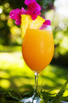 A Tropical Cocktail Garnished With Fruit In An Outdoor Setting.