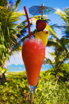 A Tropical Cocktail Garnished With Fruit In An Outdoor Setting.