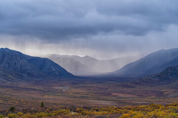 Rain clouds over mountains along the Dempster Highway create amazing landscapes while fall colors settle into the valley; Yukon, Canada