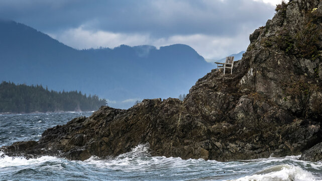 A wooden bench sits on a rugged rock slope with a view of the rugged coastline at Brady's Beach in Bamfield, Vancouver Island; Bamfield, British Columbia, Canada