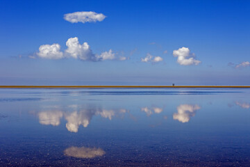a smooth lake reflects clouds and a blue sky with a stretch of land in the middle