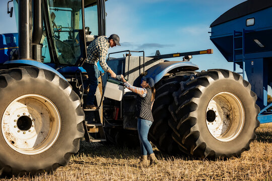 A wife brings her husband lunch at the cab of a tractor while being busy with the fall, canola harvest; Alcomdale, Alberta, Canada