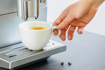 Female hand taking of cup of fresh hot espresso pouring from coffee machine. Professional coffee brewing. Cup of natural espresso. Coffee break. Good morning. Life style. Soft focus