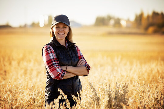 Portrait of a mature farm woman standing in a grain field, posing for the camera during harvest at sunset; Alcomdale, Alberta, Canada