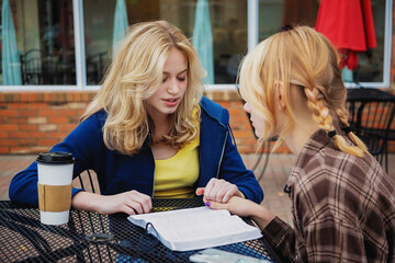 Two teenagers spending time praying together at an outdoor cafe after reading and studying the Bible; St. Albert, Alberta, Canada