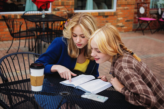 Two teenagers spending quality time together at an outdoor cafe and reading and studying the Bible; St. Albert, Alberta, Canada