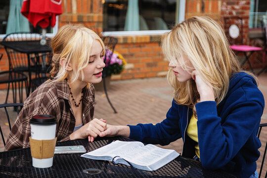 Two teenagers spending time praying together at an outdoor cafe after reading and studying the Bible; St. Albert, Alberta, Canada