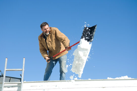 Man shovels snow off a roof with a shovel after a snowstorm; Lincoln, Nebraska, United States of America