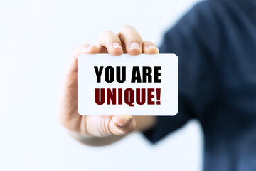 You are unique text on blank business card being held by a woman's hand with blurred background. Business concept about uniqueness.