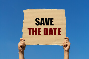 Save the date text on box paper held by 2 hands with isolated blue sky background. This message board can be used as business concept about reserve the date.