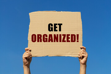 Get organized text on box paper held by 2 hands with isolated blue sky background. This message board can be used as business concept about you getting organized.