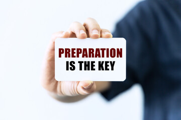 Preparation is the key text on blank business card being held by a woman's hand with blurred background. Business concept about preparation.