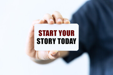 Start your story today text on blank business card being held by a woman's hand with blurred background. Business concept about starting your story.