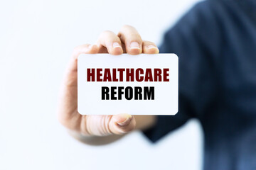 Healthcare reform text on blank business card being held by a woman's hand with blurred background. Business concept about healthcare reform.