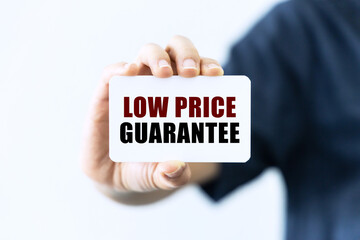 Low price guarantee text on blank business card being held by a woman's hand with blurred background. Business concept about price.