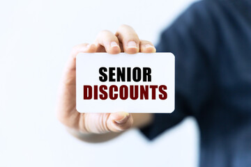 Senior discounts text on blank business card being held by a woman's hand with blurred background. Business concept about discount.