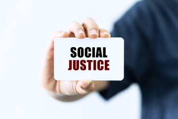 Social justice text on blank business card being held by a woman's hand with blurred background. Business concept about social justice.