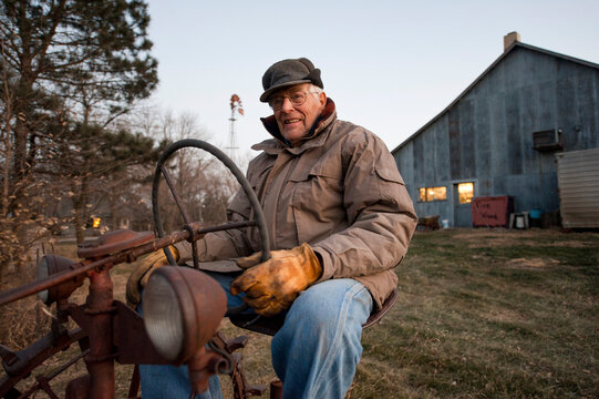 Senior man sits on an antique tractor on a farm; Cortland, Nebraska, United States of America