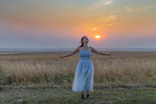 Dancer stands with arms outstretched on the prairies at sunset; Three Hills, Alberta, Canada