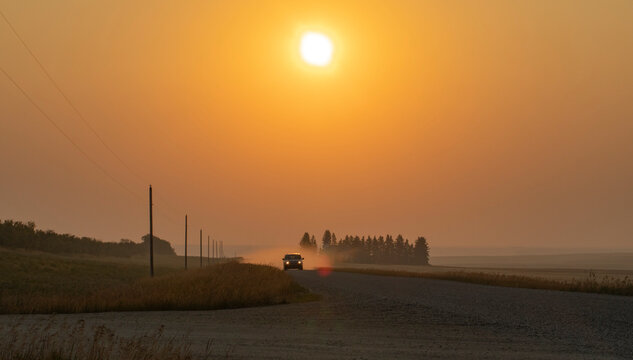 Driving down a country road in golden sunlight and a glowing orange sky; Alberta, Canada