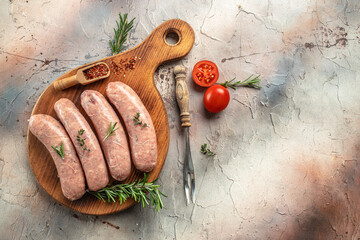 Raw sausages on a wooden cutting board with tomatoes and herbs on a light background. place for...